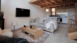 Una sala de estar moderna con un sofá gris, una mesa de centro de madera y un televisor de pantalla plana montado en la pared.