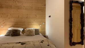 Un dormitorio con techo de madera, cama con ropa de cama blanca y marrón, y espejo con marco ornamentado.