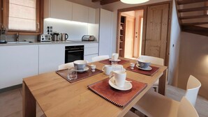 Una cocina moderna con vigas de madera, una mesa de comedor con platos y tazas blancos, y vista a una puerta de madera que da a otra habitación.