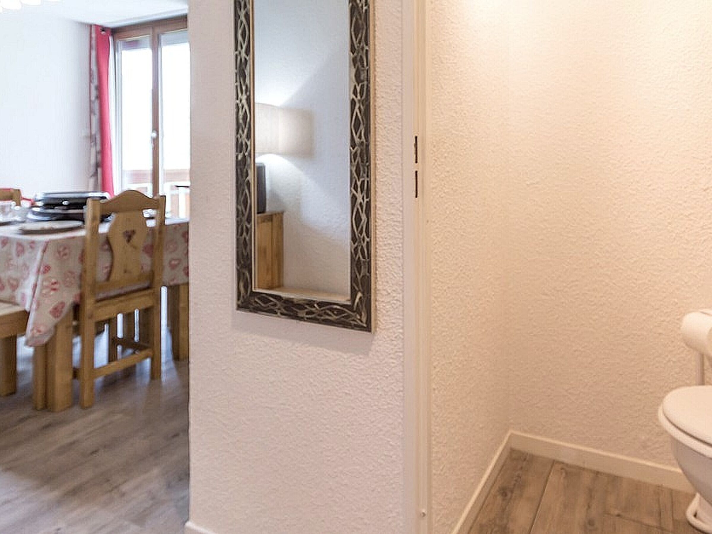 A room with a wooden dining table, chairs, a white toilet, and a mirror with a decorative frame.