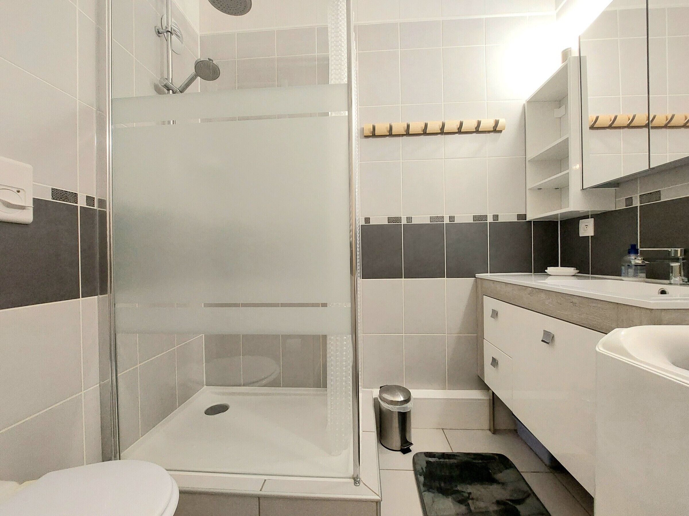 A modern bathroom with a glass-enclosed shower, a toilet, a sink, and a trash bin.