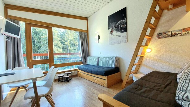 Een gezellig houten chalet interieur met een eettafel, stoelen, een bank en een ladder.