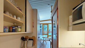 Een smalle keuken met een magnetron, spoelbak en open wandplanken met keukengerei.