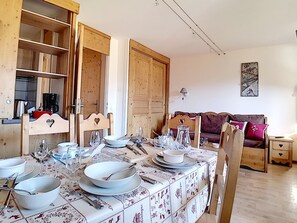 Un coin repas avec une table dressée pour quatre personnes, des meubles en bois, un canapé et une lampe fixée au mur.