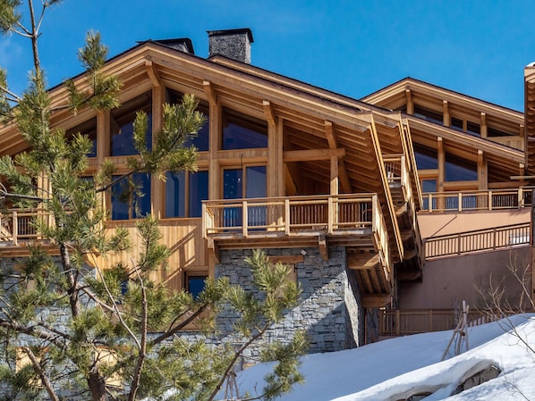 A multi-story wooden building with large windows, a stone foundation, and a wooden staircase leading to a balcony.