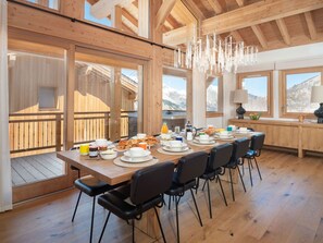A dining area with a long wooden table set for breakfast, large windows with mountain views, and a wooden ceiling structure. - Luxury ski-in chalet with sauna and hot tub in Saint-Martin-de-Belleville (Saint-Martin-de-Belleville)
