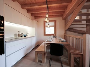 Eine moderne Küche mit weißen Schränken, einem Holzespeisetisch für vier Personen und einer Treppe mit hölzernen Geländern.