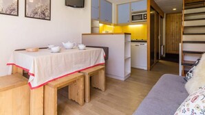Una habitación acogedora con un banco y una mesa de madera, una zona de cocina con microondas y un televisor montado en la pared.