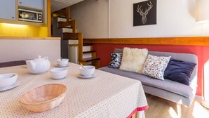 Una habitación acogedora con una mesa de comedor lista para cuatro personas, un sofá con cojines estampados, un cuadro de un ciervo colgado en la pared y una escalera que conduce a un nivel superior.