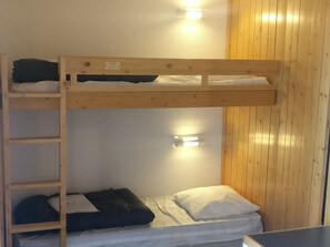 Ein Schlafraum mit Etagenbetten, einer Holzleiter und einer Wandleuchte.