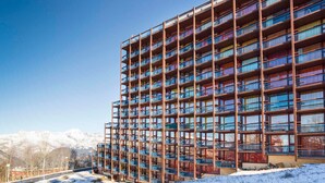 A multi-story hotel with a grid of balconies, set against a snowy mountain backdrop.