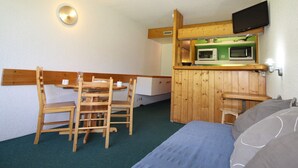 A compact room with a bed, a wooden desk, a chair, a microwave, and a television mounted on the wall.