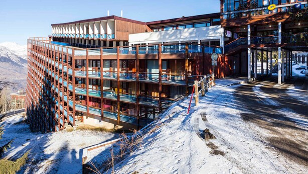 A multi-story hotel with balconies and a ski resort backdrop.