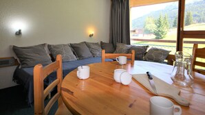 A cozy room with a wooden table, chairs, a sofa, and a window with a view of mountains.