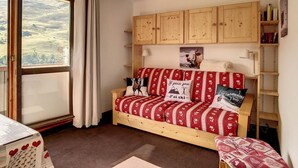 A cozy room with a wooden sofa, a view through a large window, and a wooden cabinet with a picture on the wall.