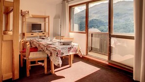 A dining area with a table set for four, a television, and a view of a mountainous landscape through large windows.