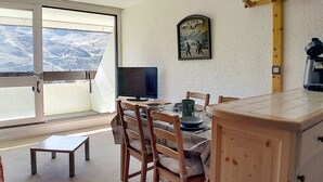 Un comedor con una mesa, sillas, un televisor y vistas a la montaña a través de un gran ventanal.