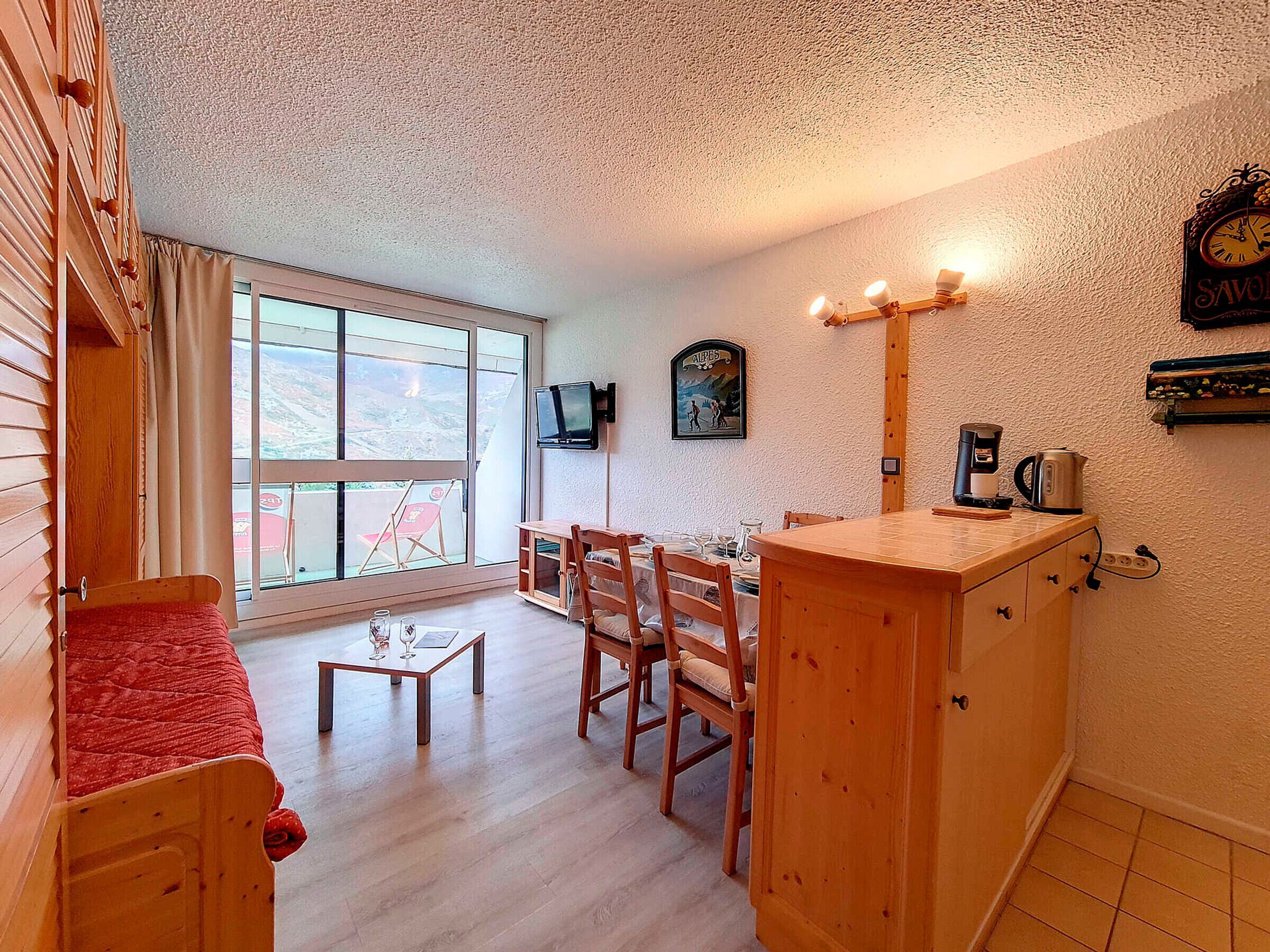 Une pièce chaleureuse avec un lit en bois, une petite table avec des verres, une table à manger avec des chaises, un téléviseur fixé au mur et une horloge.