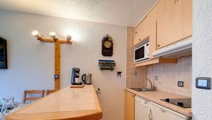 Una cocina con una mesa de madera, una cafetera, un hervidor, un microondas y un reloj en la pared.
