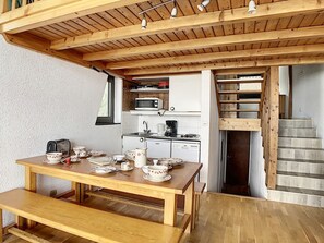 Un tavolo da pranzo in legno apparecchiato con piatti, tazze e un bollitore. Sullo sfondo, si vede una cucina con microonde, macchina del caffè e lavastoviglie.