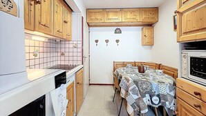 Una cocina compacta con armarios de madera, salpicadero de azulejos, una mesa de comedor con mantel estampado y horno empotrado.