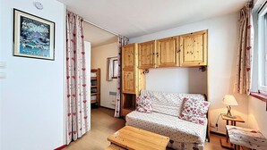 Una habitación acogedora con sofá, armarios de madera, una mesita y una ventana con cortinas.