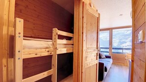 A wooden interior with bunk beds and a view of a snowy landscape through large windows.
