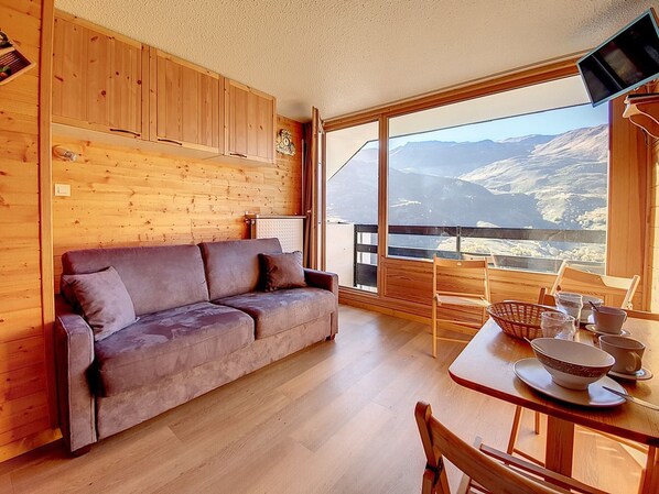 Une pièce chaleureuse avec un mur en bois, un canapé, une table à manger avec des chaises et une grande fenêtre donnant sur un paysage montagneux.