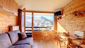 A cozy room with a sofa, dining table, chairs, and a TV.