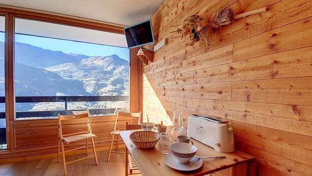 A wooden cabin with a dining area, a television, and a view of mountains.