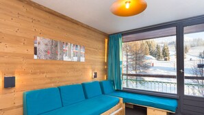 Een houten interieur met een blauwe bank, een raam met uitzicht op een besneeerd landschap en een hanglamp.