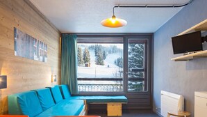 Een moderne kamer met een houten wand, een blauwe bank, een eettafel en een raam met uitzicht op een besneeerd landschap.