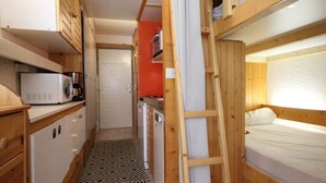 Un intérieur compact en bois, comprenant un coin cuisine, un lit et une échelle.