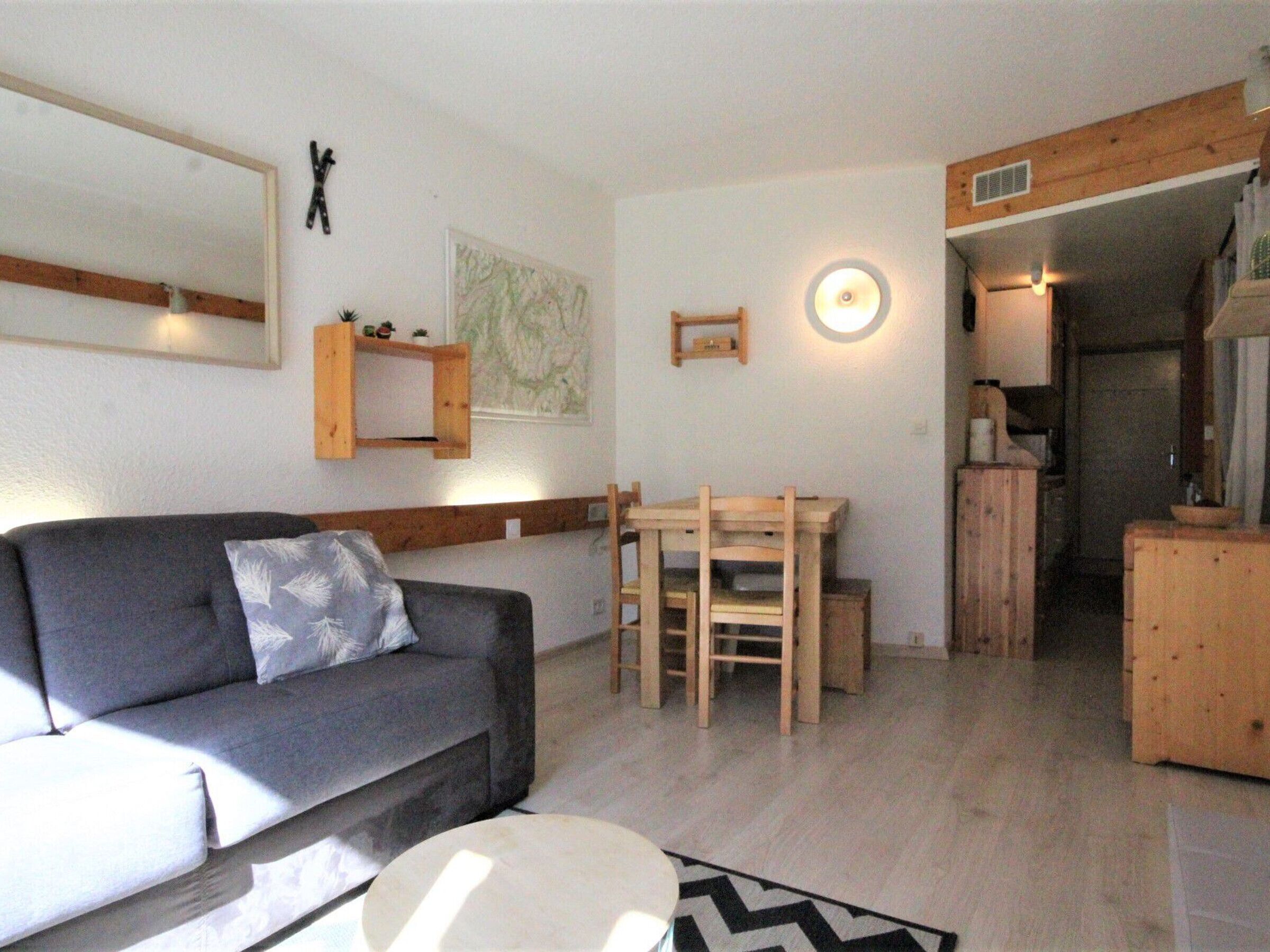 Una sala de estar con un sofá gris, una mesa de comedor de madera con sillas, un mapa en la pared y un mueble bajo.