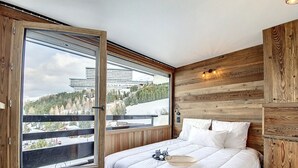 A bedroom with a large sliding glass door leading to a balcony, a bed with white bedding, and wooden paneling on the walls.