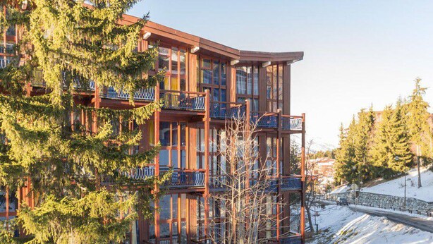 A multi-story building with balconies, surrounded by snow and trees.