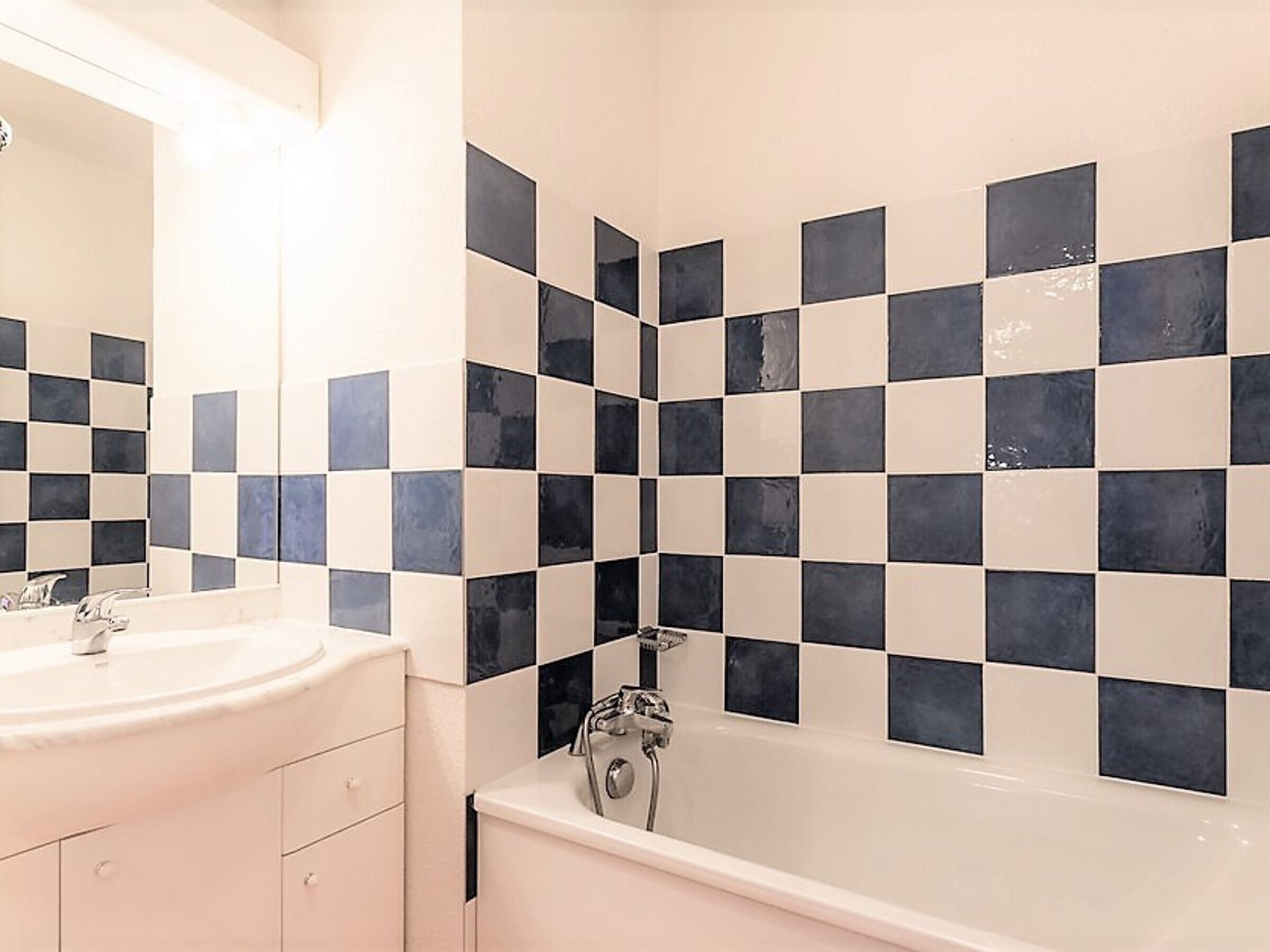 Ein Badezimmer mit Wand aus Schachbrettfliesen, einem weißen Waschbecken und einer Badewanne.