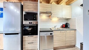 Una cucina compatta con elettrodomestici integrati, pensili in legno e zanzariera piastrellata.