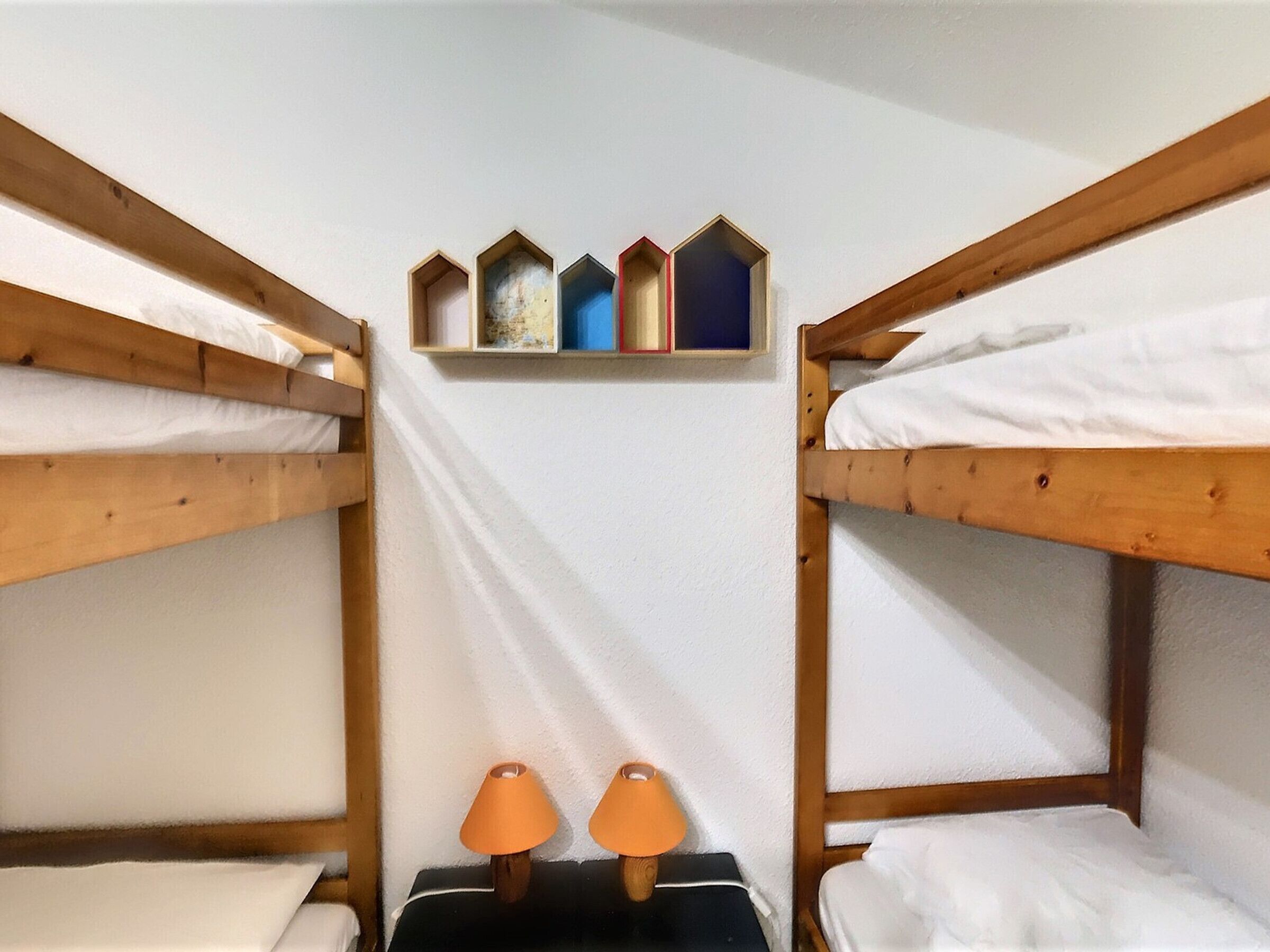 Habitación con literas, dos lámparas de noche y una estantería decorada.
