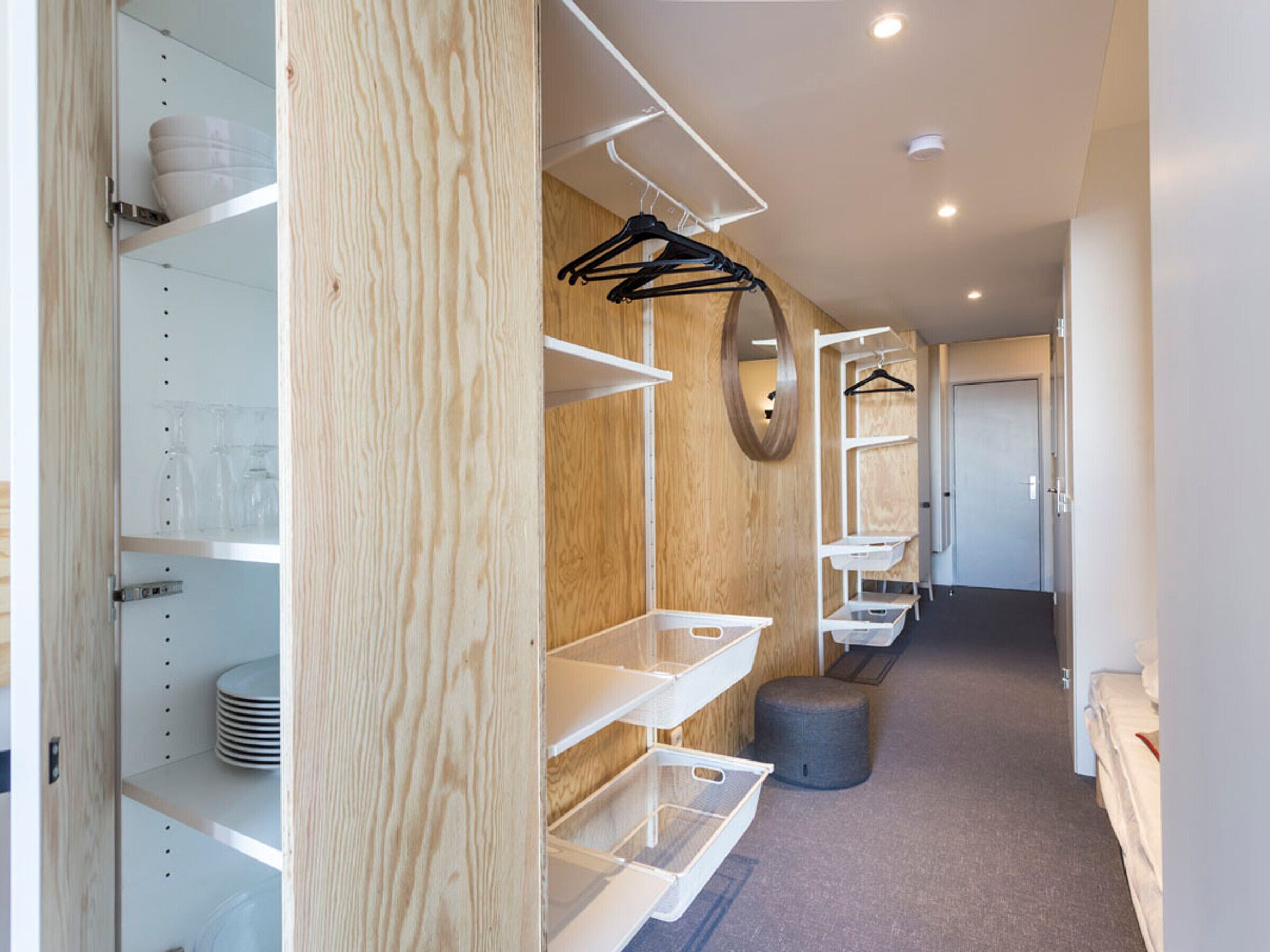 Ett modernt hotellrum med hyllor i trä, en spegel och en minimalistisk design.