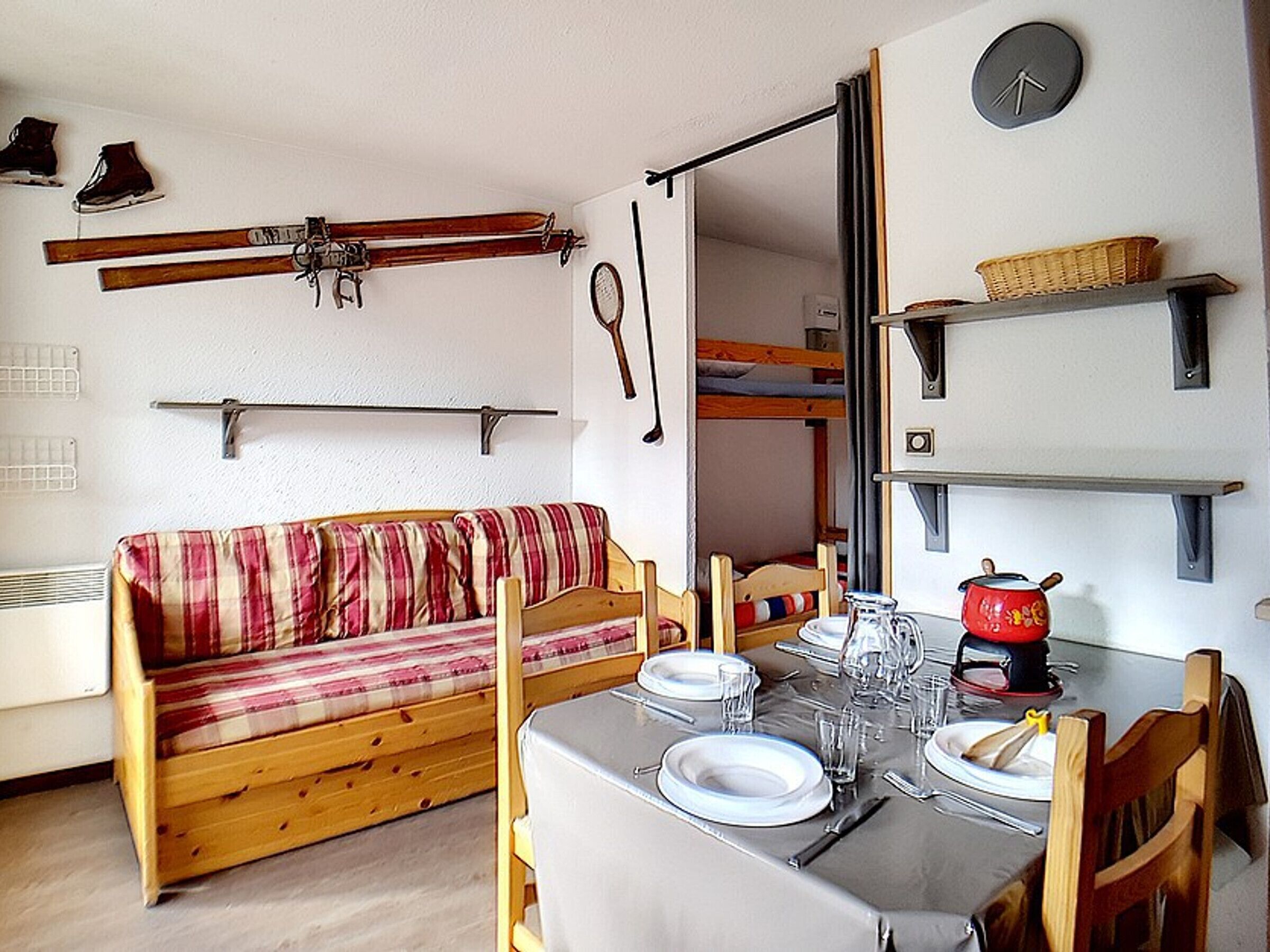 A compact living space with a sofa, dining table set for two, and a bunk bed in the background.