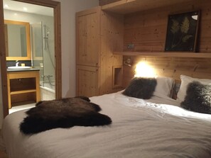 A bedroom with a wooden headboard, a bed with white linens, a fluffy pillow, a bedside table, and a mirror above the sink.