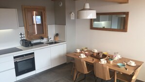 A modern kitchen with white cabinets, a built-in oven, and a wooden dining table set with white plates and cups.