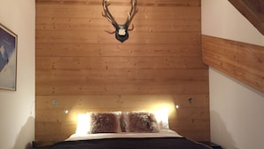 A bedroom with a wooden ceiling, a bed with a dark blanket, and a mounted deer skull above the bed.