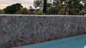 Ein Schwimmbecken mit Steinwänden und gefliesten Rändern, umgeben von Grünflächen.