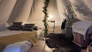 Ein Zelt mit Bett, Kissen, Decke, einem kleinen Tisch mit Pflanze und einem Stuhl.