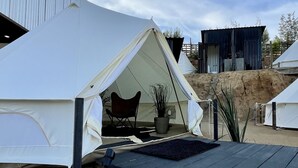 Ein Campingplatz mit Zelten, einer schwarzen Plattform, einem Stuhl und einem Blumentopf.