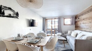Un salon moderne comprenant un coin repas, des murs en bois, un téléviseur à écran plat et une grande fenêtre avec des rideaux.