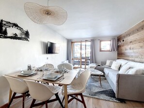 Ein modernes Wohnzimmer mit Essbereich, Holzwänden, einem Flachbildfernseher und einem großen Fenster mit Vorhängen.
