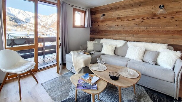 Un salon moderne avec un canapé, une table basse et un fauteuil. Une grande fenêtre offre une vue sur les montagnes.